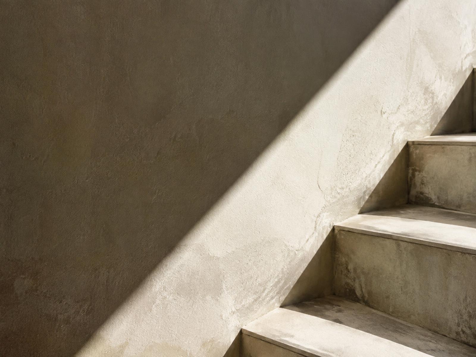 Concrete stair and limewashed wall cut by a diagonal shaft of light